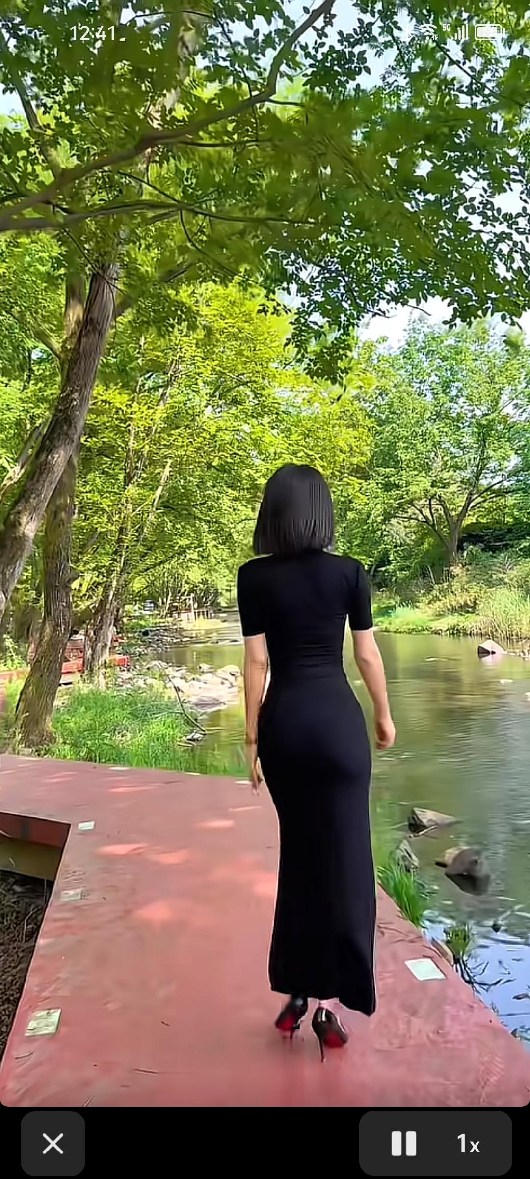 一个穿黑裙子的女人漫步在绿意盎然的湖畔，尽享自然之美。