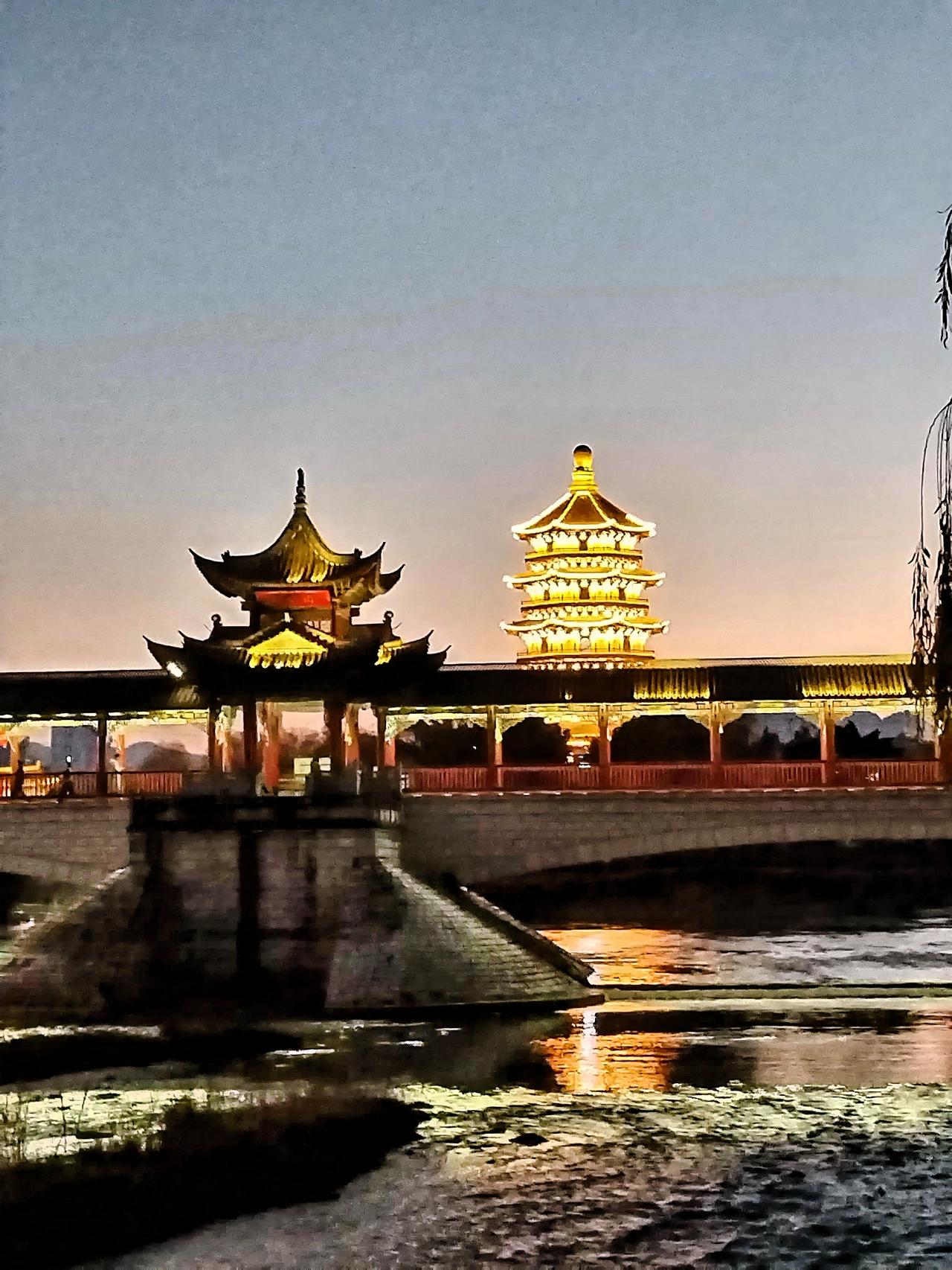 夜幕笼罩，古塔与廊桥在灯光映照下，宛如梦幻之境。步入这如梦似幻的夜色，古塔的轮廓