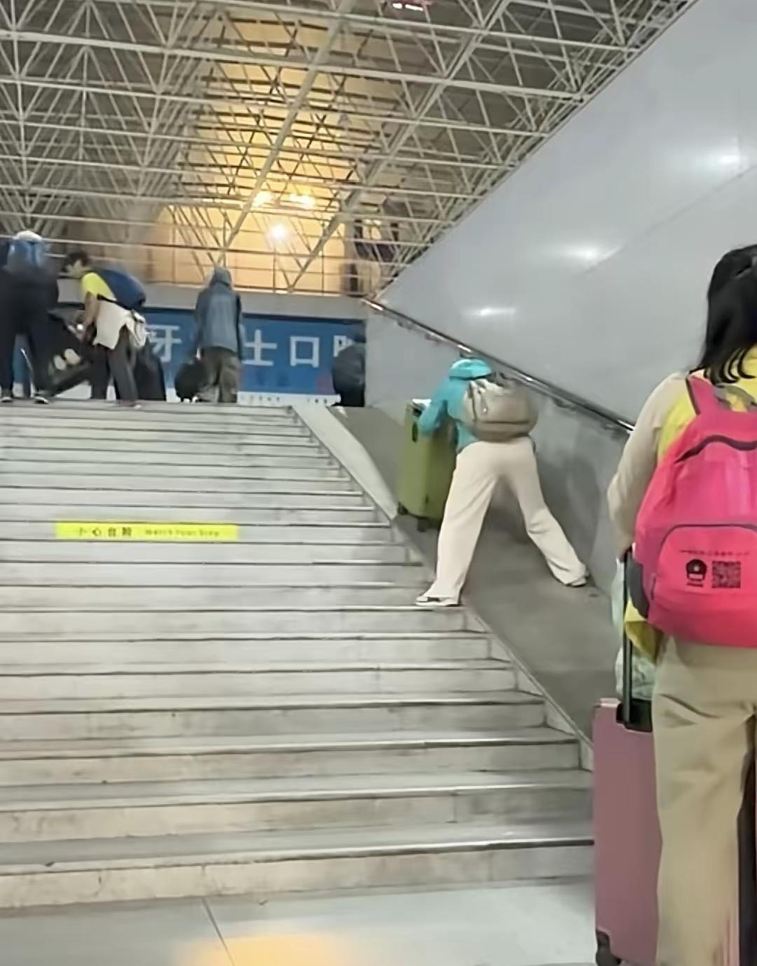 火车站里，一名女子拖着沉甸甸的行李箱，在斜坡上费劲往上挪，身子往前倾，看着就特别