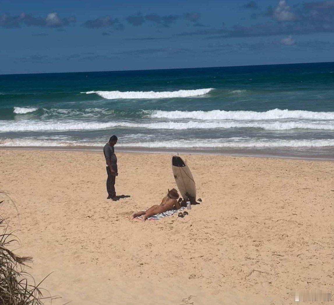 澳大利亚昆士兰，一名独自来冲浪的女性躺在一处空旷的海滩上，一个印度人走过来一直站