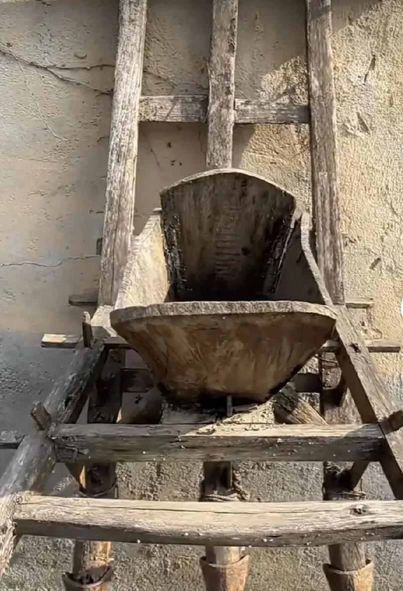 这破旧却造型独特的老物件，静静待在角落。它有着木质的框架和奇怪的斗状结构，底部还
