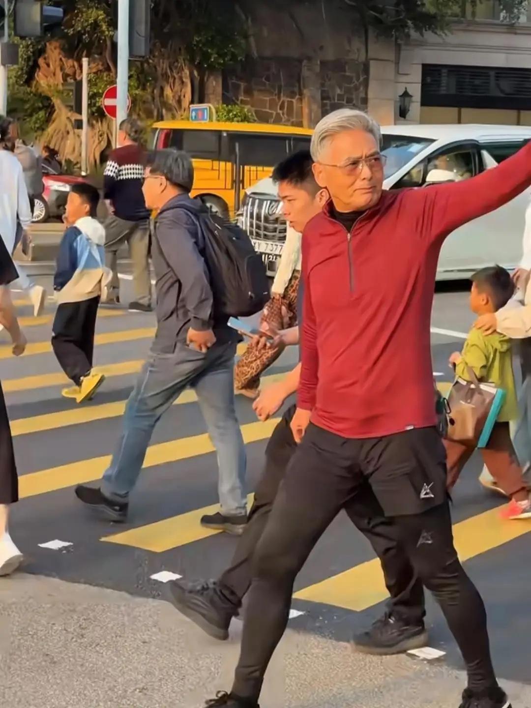 70岁周润发现身香港街头，他穿着红色运动衫下配黑色修身裤，一头白发梳得一丝不苟，