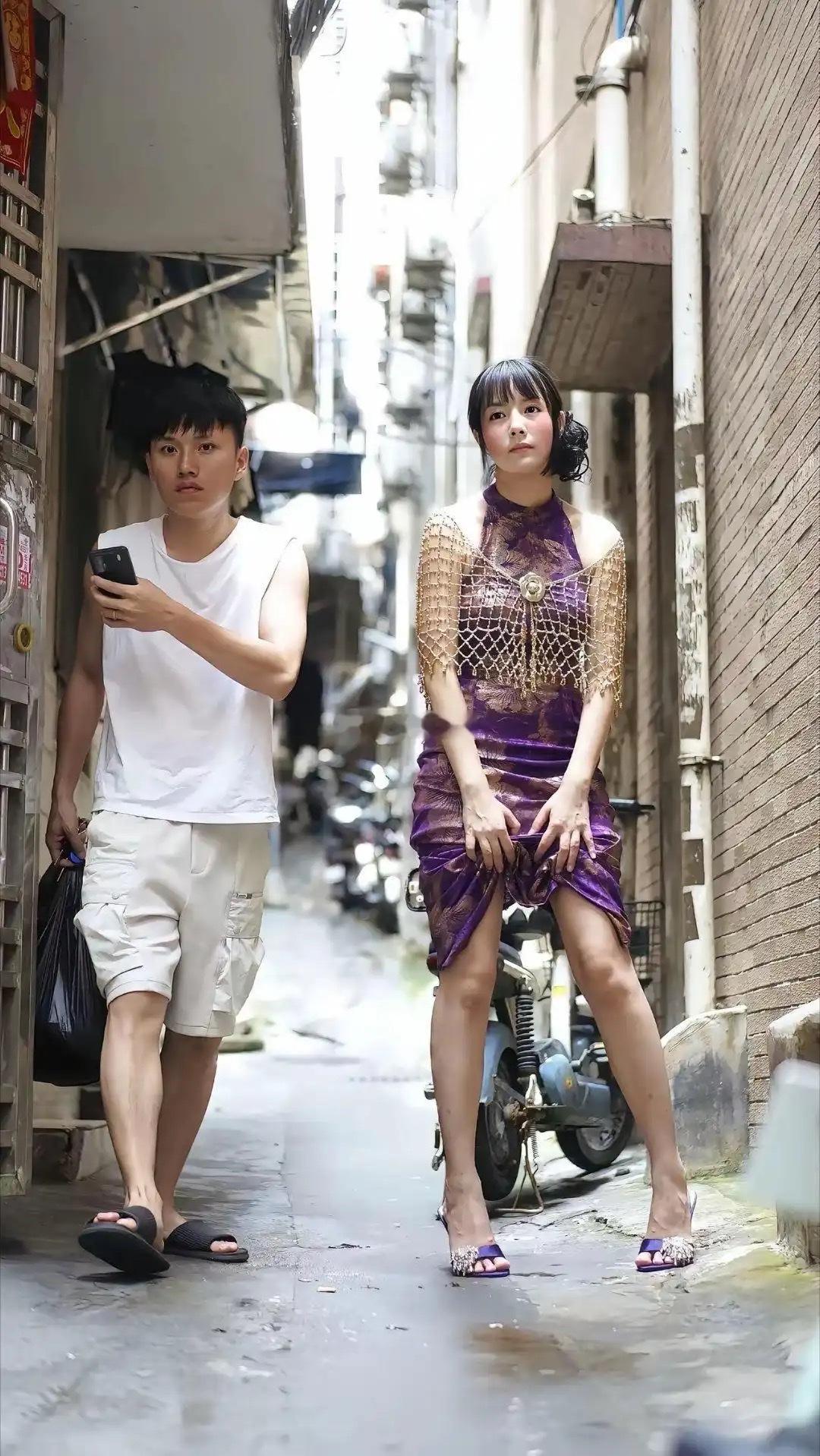 城中村老巷纪实拍摄，一身华贵紫色旗袍搭配精致金披肩，与老旧街巷形成强烈反差。昔日