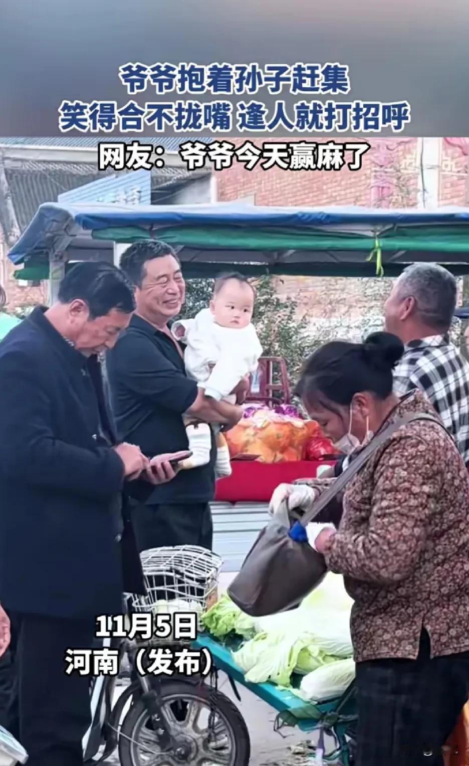 河南一爷爷抱着孙子赶集，笑得合不拢嘴，逢人就打招呼。赶集不是目的，显摆孙子才是关