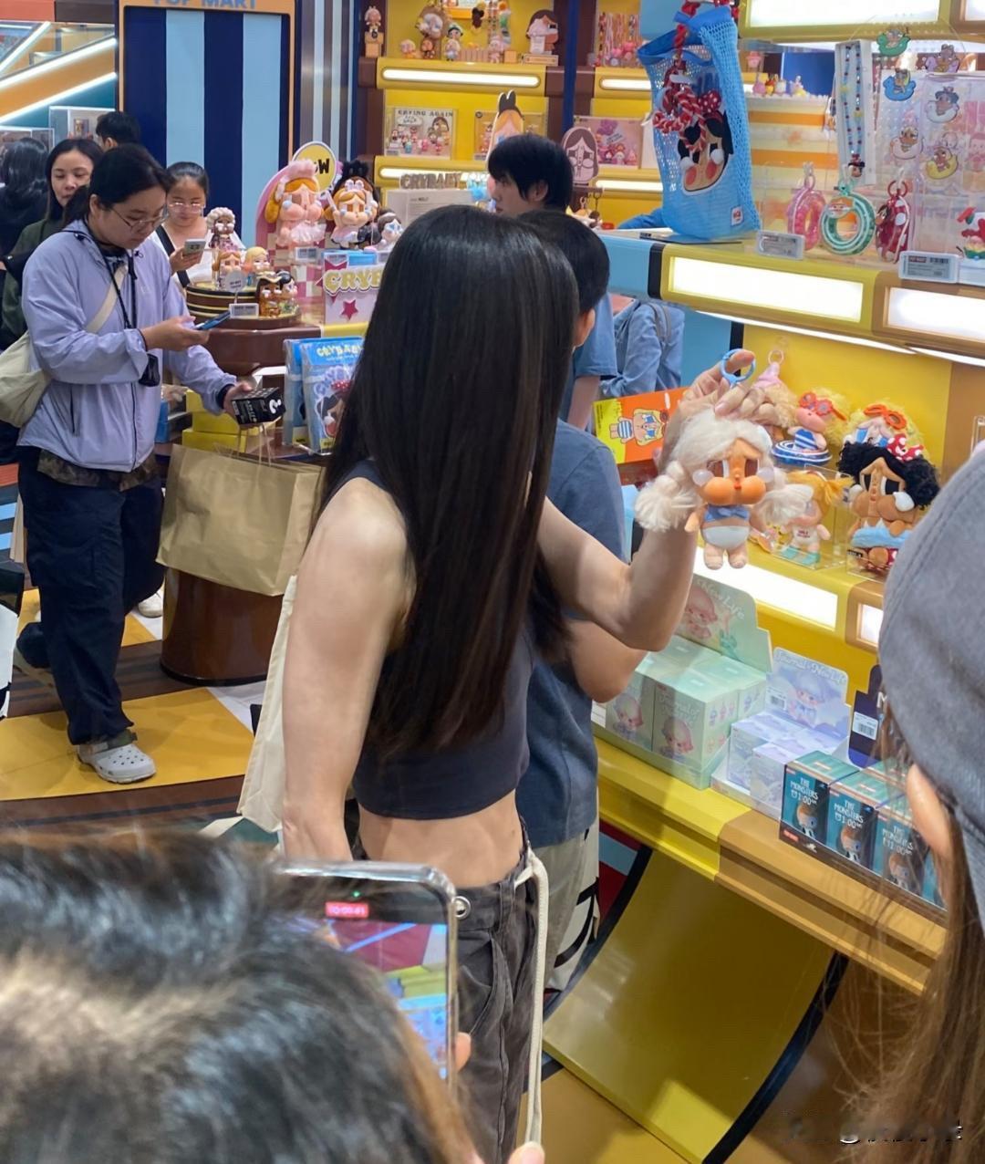 年届59岁的李若彤现身泰国的一家超市选购小玩偶。她身着露腰小背心，背部线条纤薄，