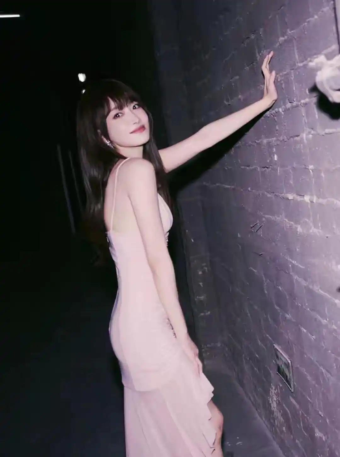 这位小姐姐穿着粉色连衣裙，站在墙边。真的是太漂亮了