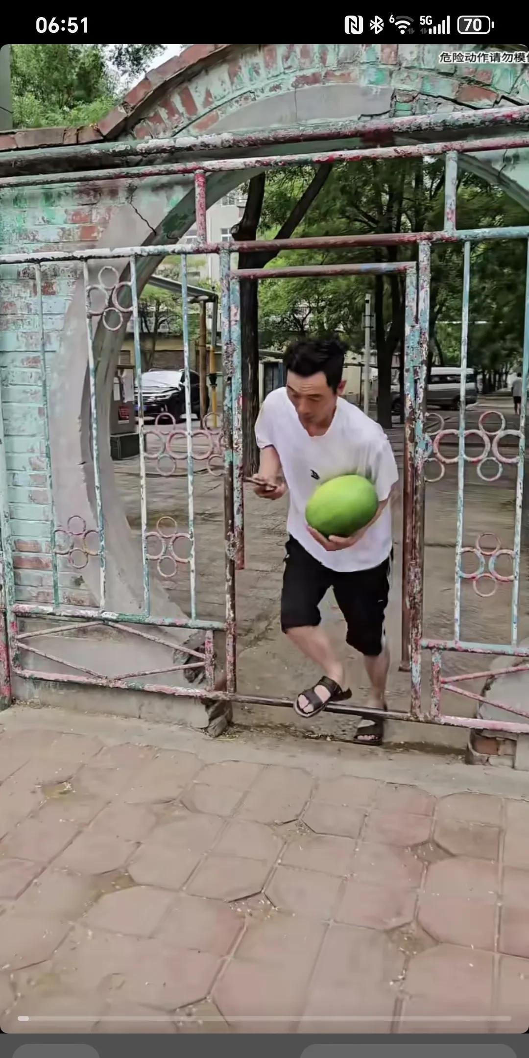 缘份让我们在此相遇～白衣男子捧着一个西瓜，边走边看手机，出小区门时不小心被门槛