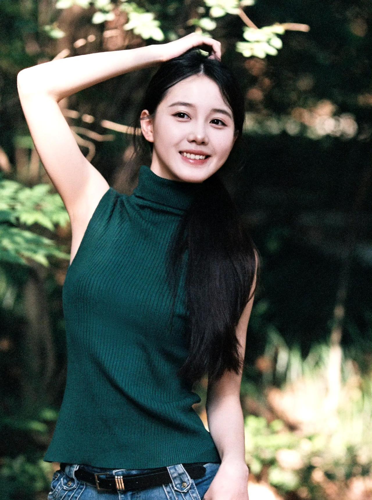 漫步林间，阳光透过叶隙洒落。她身着墨绿色无袖针织衫，搭配休闲牛仔裤，随性又自在。