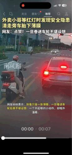 广东，外卖小哥在等红绿灯时，看到一辆汽车轮胎的边缘卷到了一块塑料膜，小哥下车，捡