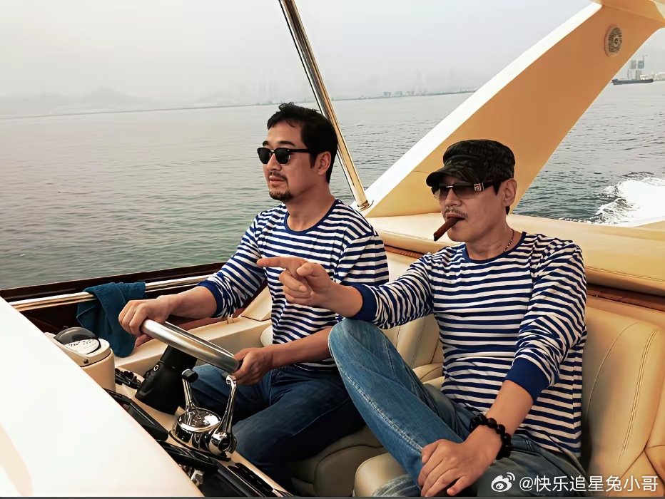 张国立与巍子二人同乘游艇出海休闲时的一幕，两人都穿着海魂衫，张国立手握方向盘，巍子叼着雪茄。​