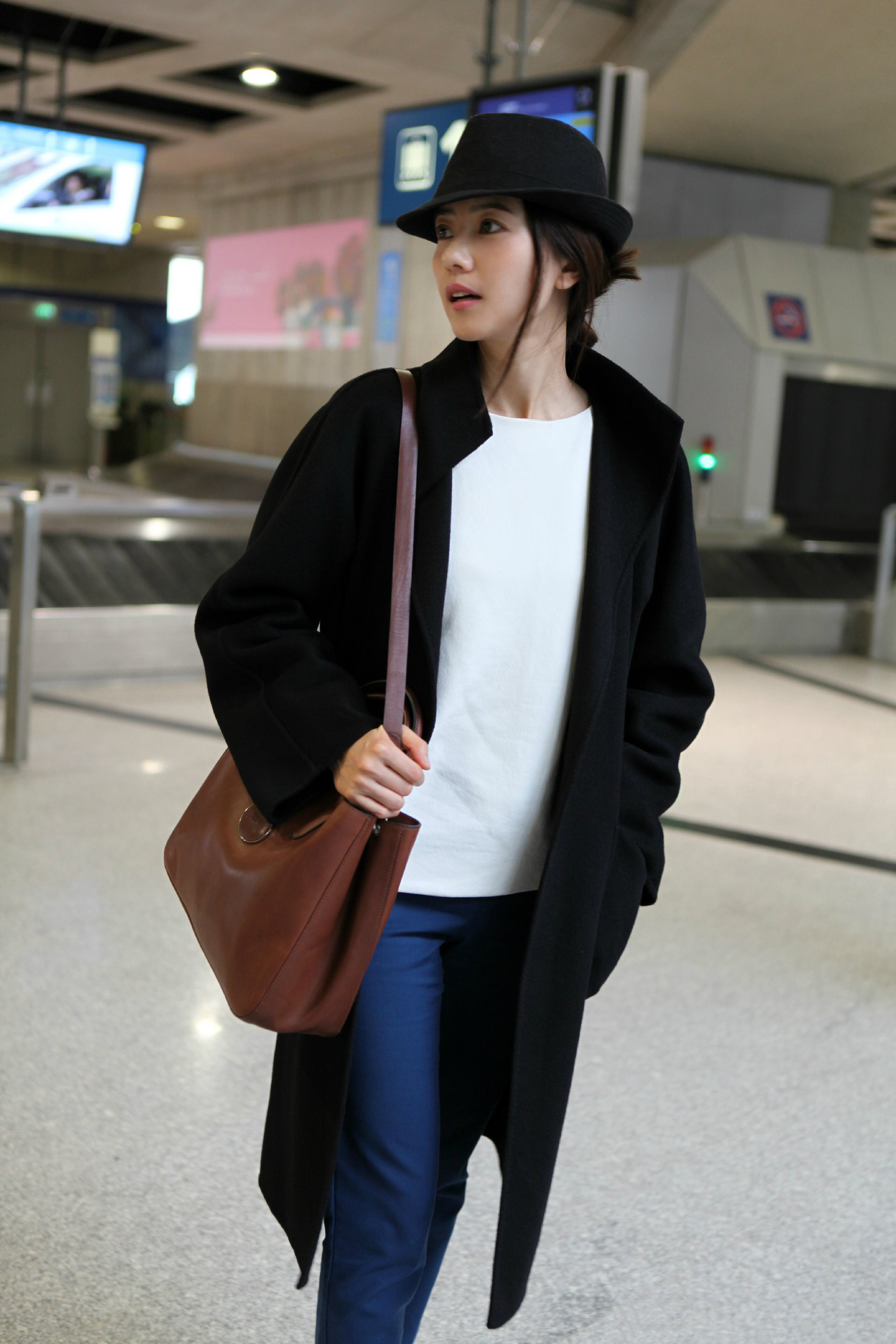这身机场穿搭堪称简约高级的范本✨。黑色礼帽与长款大衣奠定了优雅基调，内搭白衫与宝