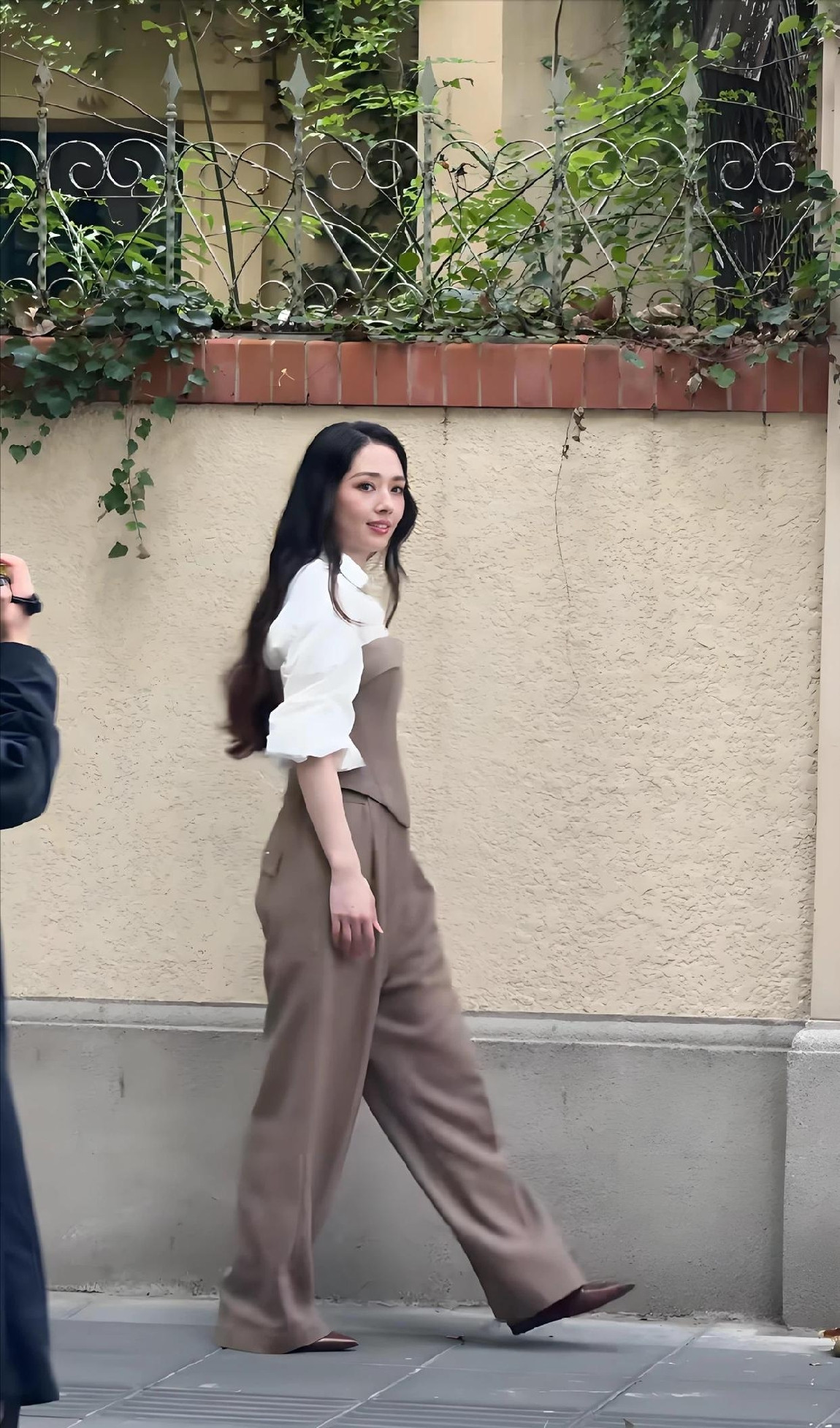 郭碧婷现身上海五原路拍片被偶遇，身穿白衬衫叠穿咖色束腰配阔腿裤，简约时尚，深色长卷发披在肩头，气质好