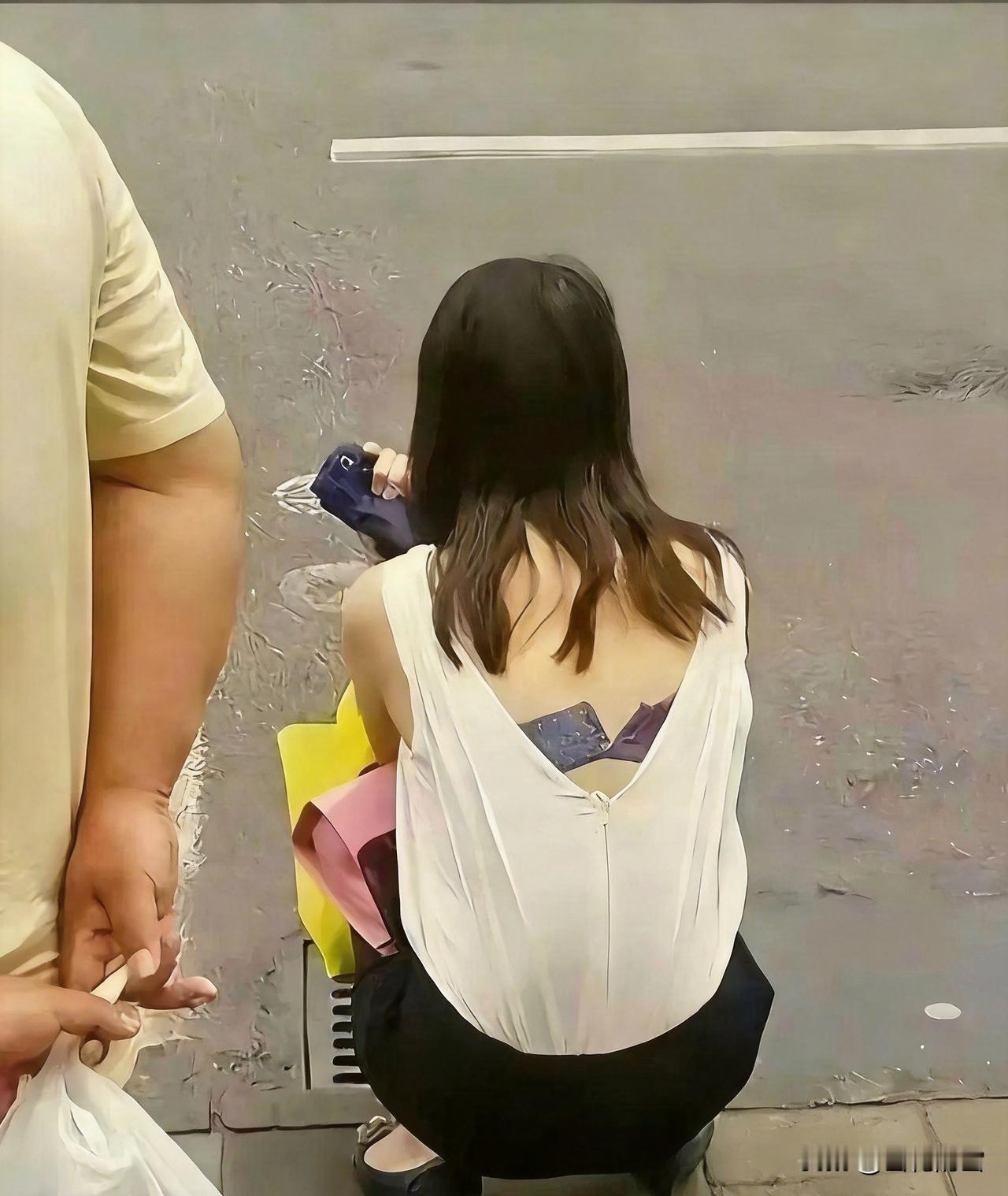 该不该去提醒一下？画面里女生蹲身时，后背上衣的拉链滑落，内里内衣清