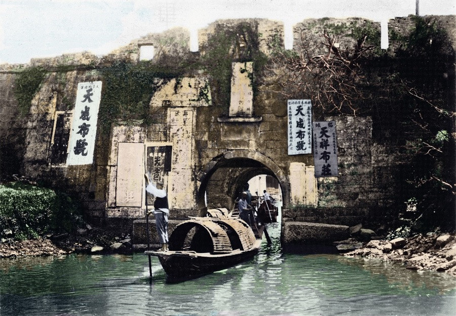 这是20世纪30年代绍兴古城墙及周边河道、乌篷船的景象。画面里，古老砖石城墙爬