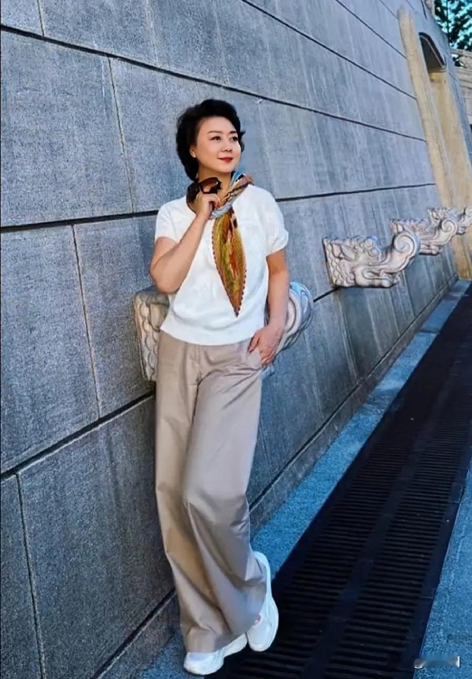 59岁李胜素和“小年轻”外出游玩，一身休闲装打扮走在街上，围着一条围巾，整个人看
