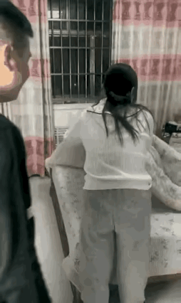 老婆家中收拾床上用品，老公从外边回来从后面紧紧抱住了她的腰说，老婆，我回来了，老