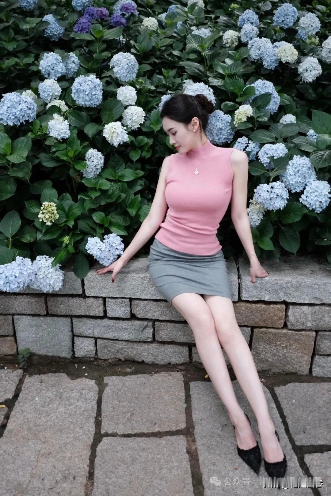 优雅气质，粉色上衣搭配灰色短裙，倚靠花丛，尽显迷人风姿。