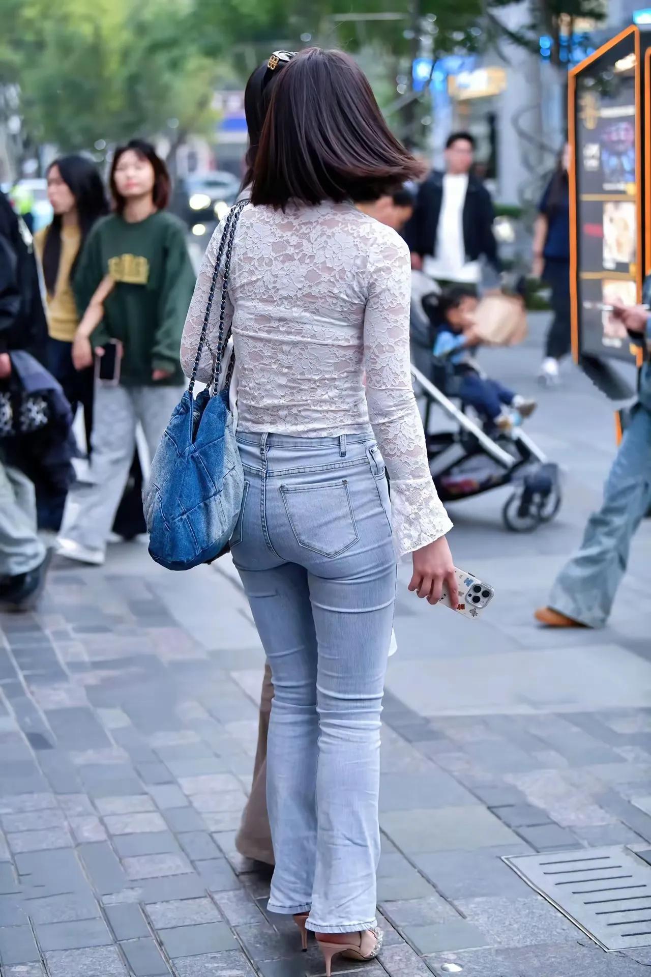 一个穿牛仔裤的女士在街上走着。经典牛仔裤要怎样搭配简约又时髦白衬衫怎么穿搭出时