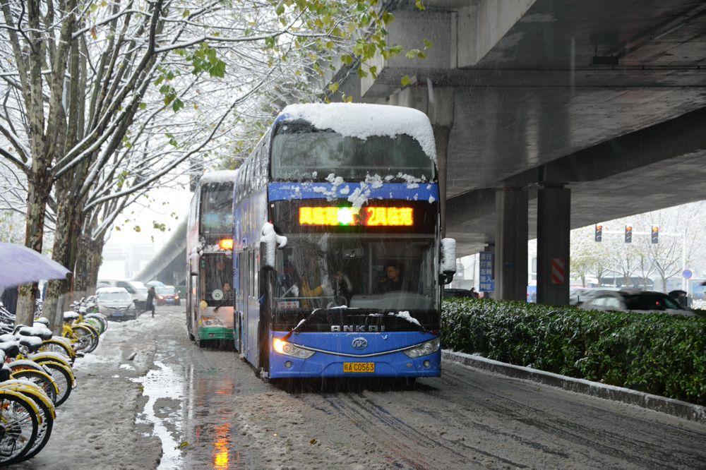 公交车缓缓驶过，车顶的积雪微微颤动，像一匹不安分的白绸。玻璃窗里，乘客们呼出的白