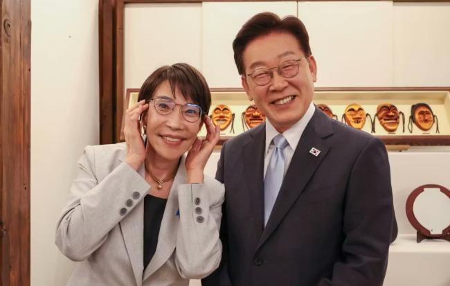 高市早苗送给韩国李在明一副眼镜，还卖萌戴着眼镜，两个人都是眯着眼睛露出牙齿笑着，