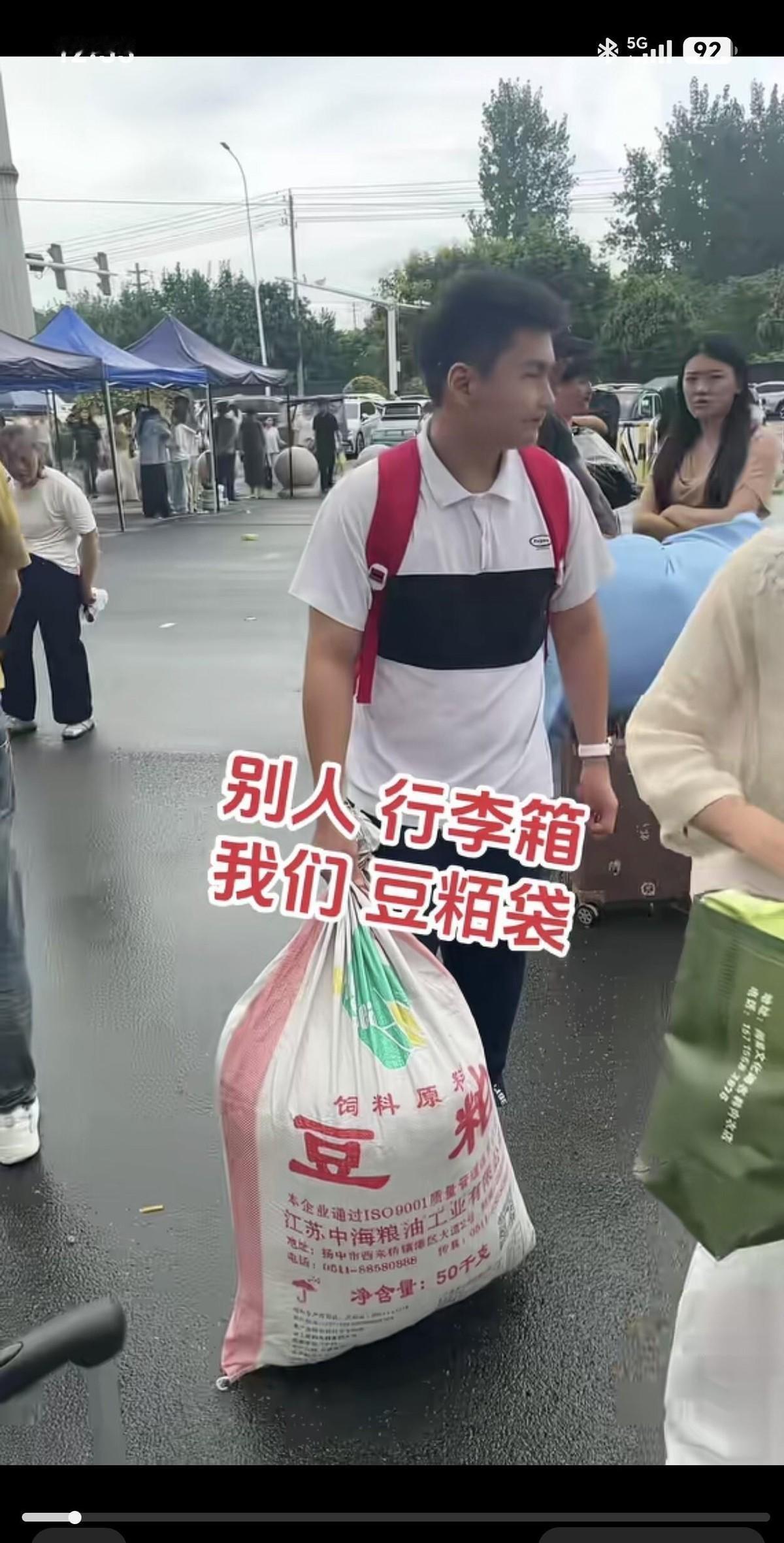 别人扛着名牌行李箱挤在新生队伍里，这个男孩把一袋豆粨往肩上一甩就进了校门。画面一