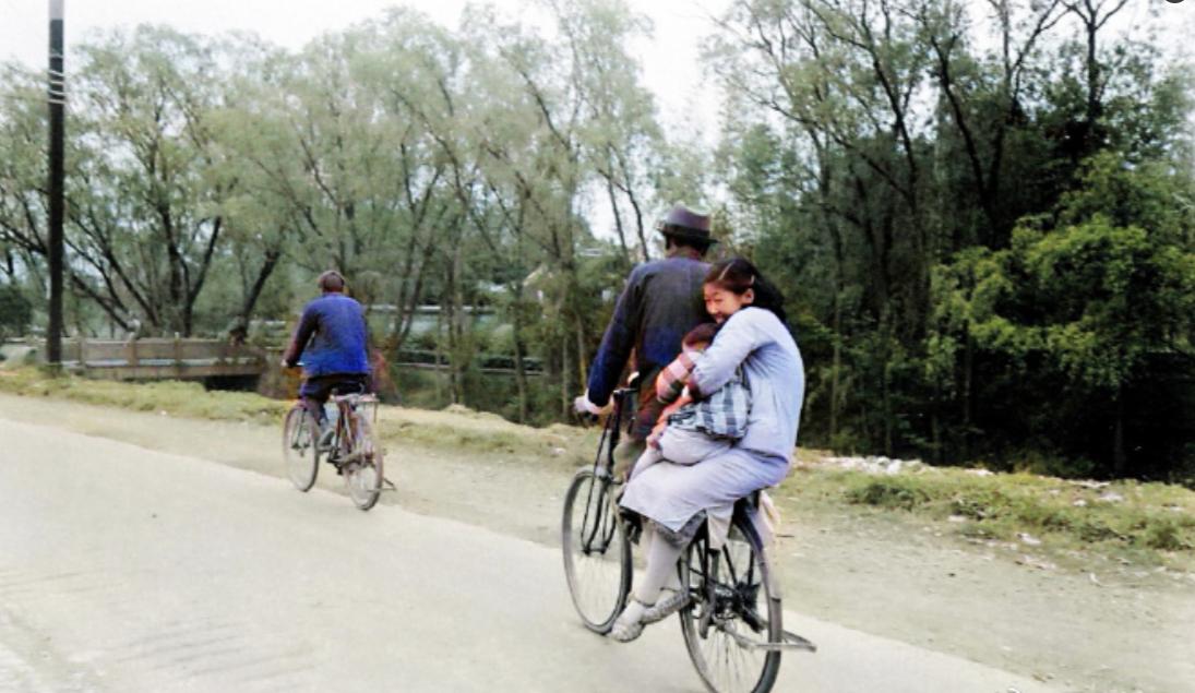 1948年上海郊区的公路上，一辆自行车载着一家人三口正前方行驶。丈夫骑着车，妻子