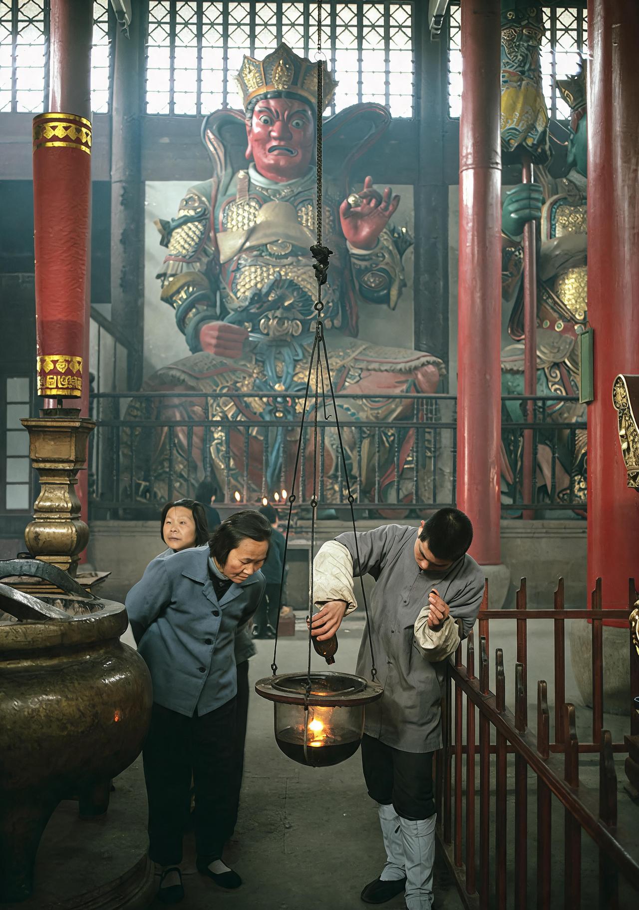 这是1983年宁波天童寺一名老太太看着一名小和尚在添灯油。小和尚手持一个油瓶向灯