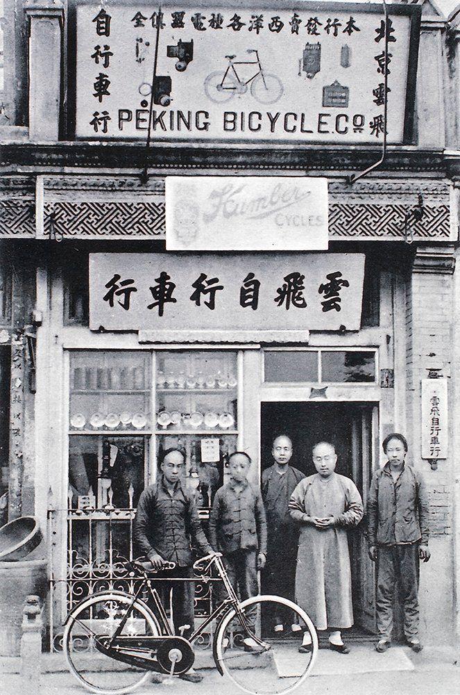 这是一张民国时期北京“云飞自行车行”的老照片。店铺门楣悬挂中英文招牌，上方绘