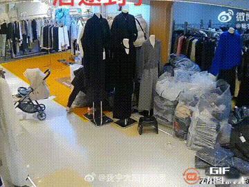 四川成都一名女子推着孩子在服装城逛街，她先是拿起摆放在门口的衣服看了看，随后见老