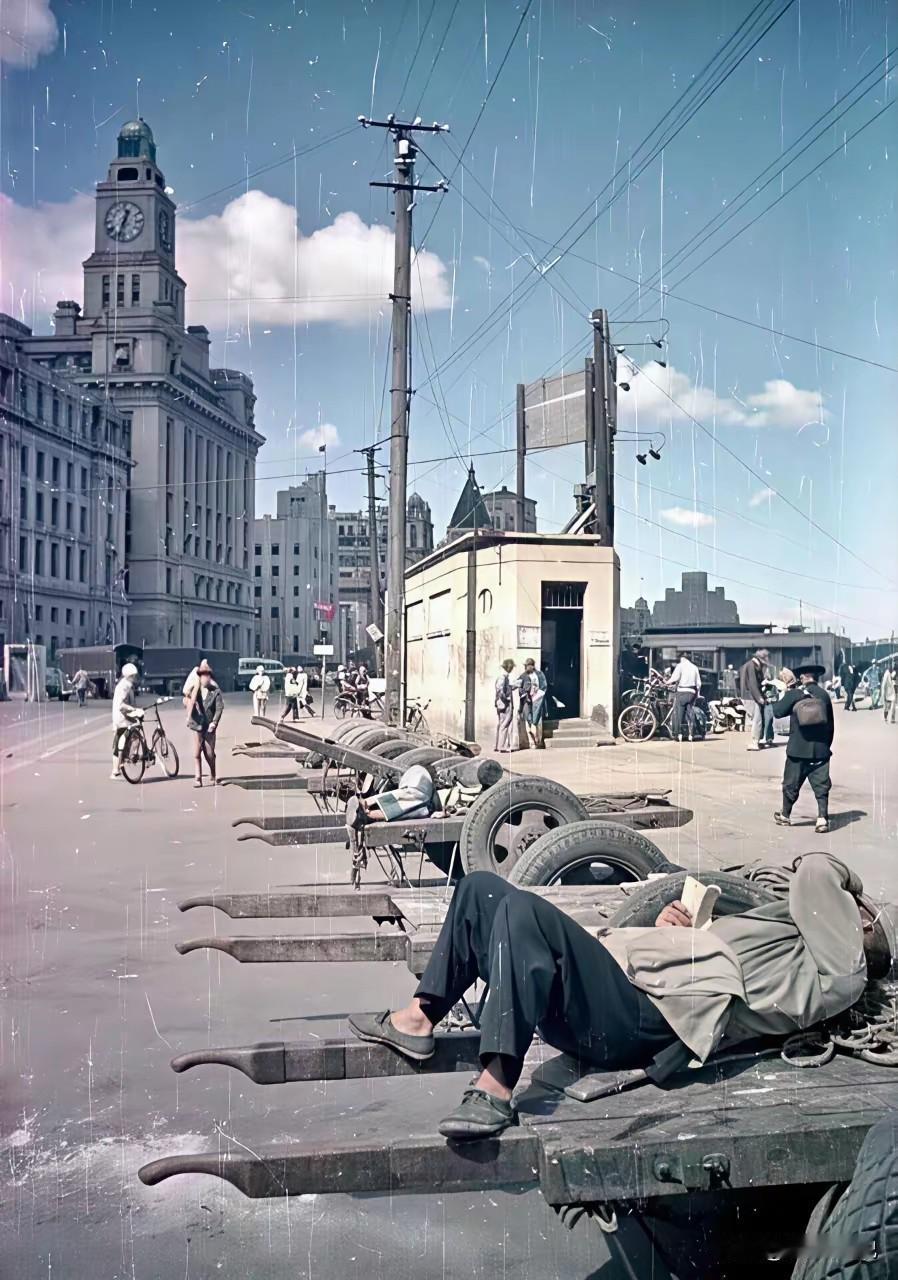 1950年，上海外滩上等活的车夫排成了一排，他们身下的平板车样子很奇特，应该是江
