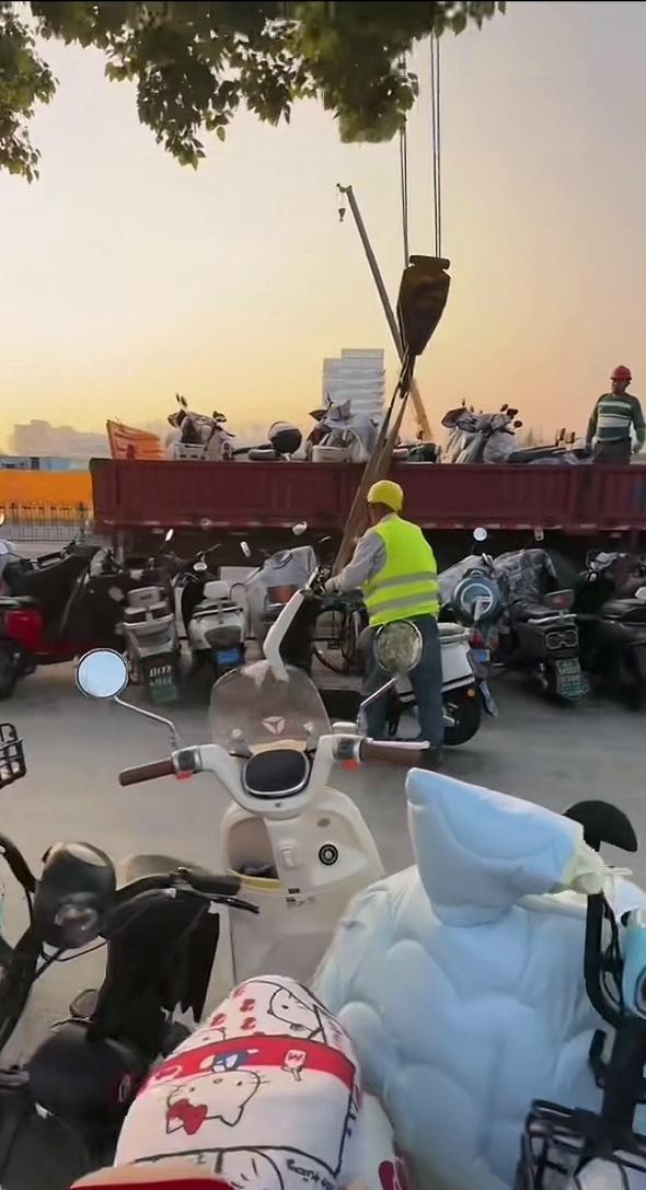 这是怎么回事呢？画面里，一辆工程车在工作人员的指挥下，正用吊钩将停在路边的电动车