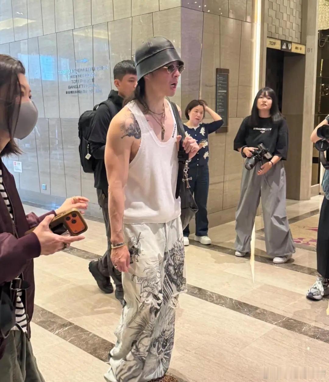 吴建豪现身深圳某酒店被偶遇，他的装扮潮酷有型，他穿着无袖上衣，留着狼尾发型，头戴