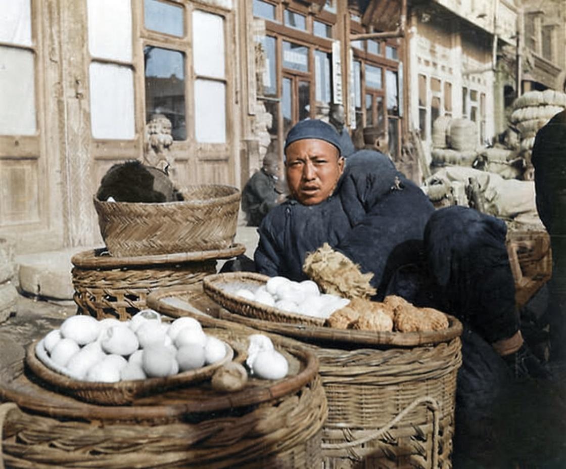 1937年，北平街头，一位小贩着厚实的棉袄在街边摆摊售卖食品，他头戴瓜皮帽，正倚