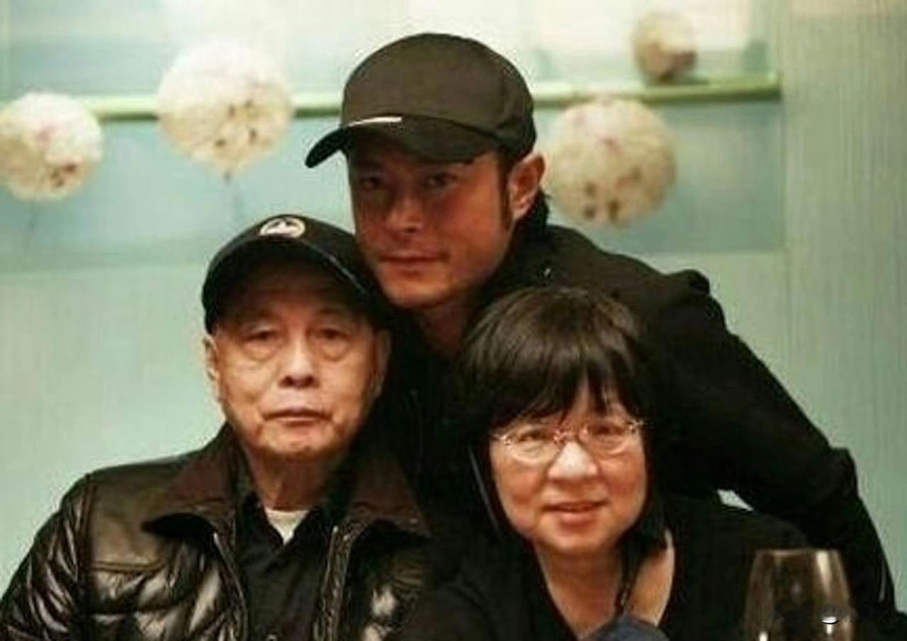 古天乐晒出全家福为妈妈庆生。他身着黑衣，双手搭在父母肩头，桌前摆着定制生日蛋