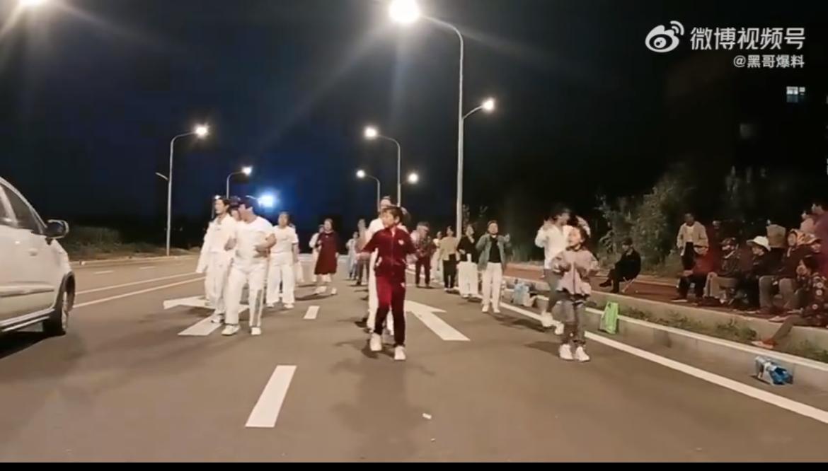 大妈们把马路当广场舞舞台，跳的不亦乐乎，队伍里面还有小孩参与。三车道被占了两车道