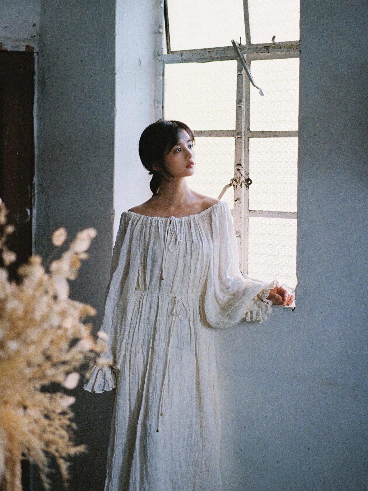 这张作品中，模特坐在铺有白色地毯的地板上，身着宽松白色针织衫，双腿自然弯曲，双手