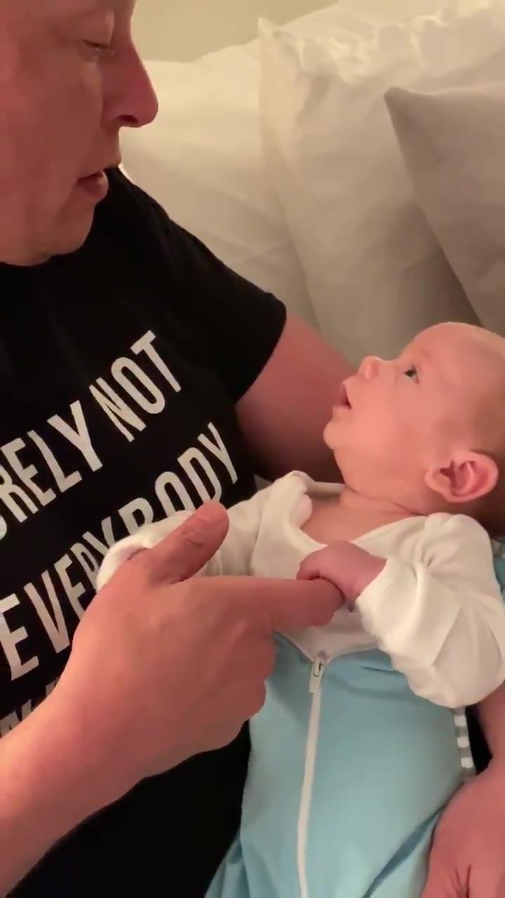 马斯克怀中的儿子看着他，这娃从小就吃得好玩得好，还有一堆哥哥姐姐陪伴他，他爸有钱