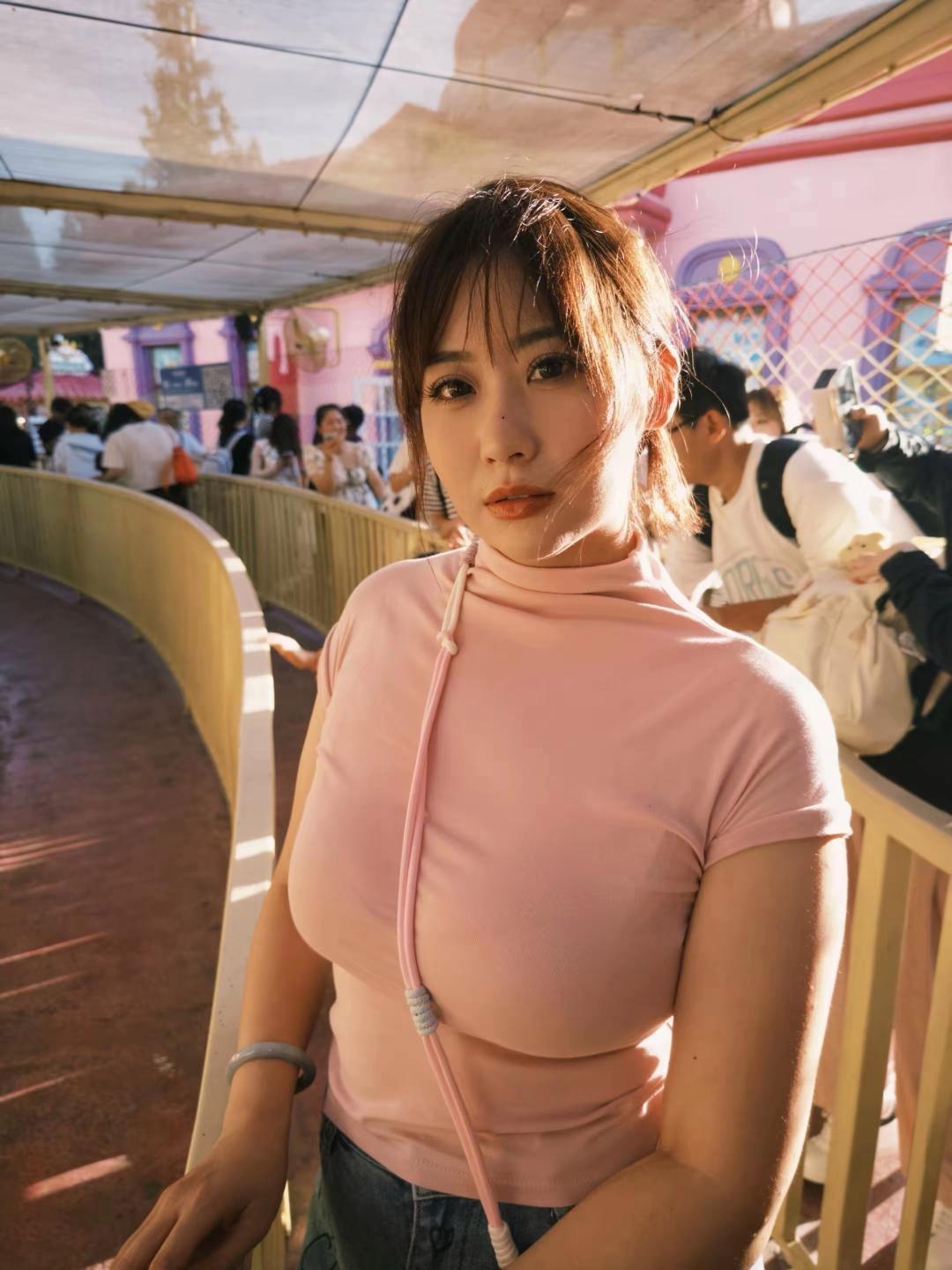 姐姐穿浅粉上衣在游乐园里，简直美到发光！暖光轻洒，发丝随风轻扬，眼眸明亮似藏星河