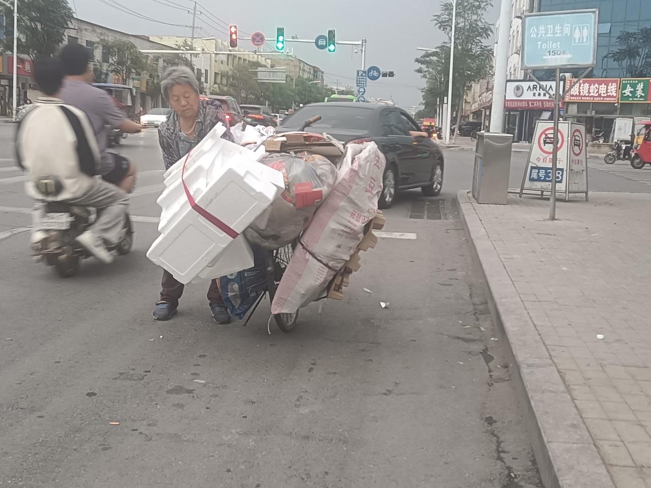 等红灯的时候，路边一个老太太站着不走了。原来，她在整理自行车上驮的废品。这一