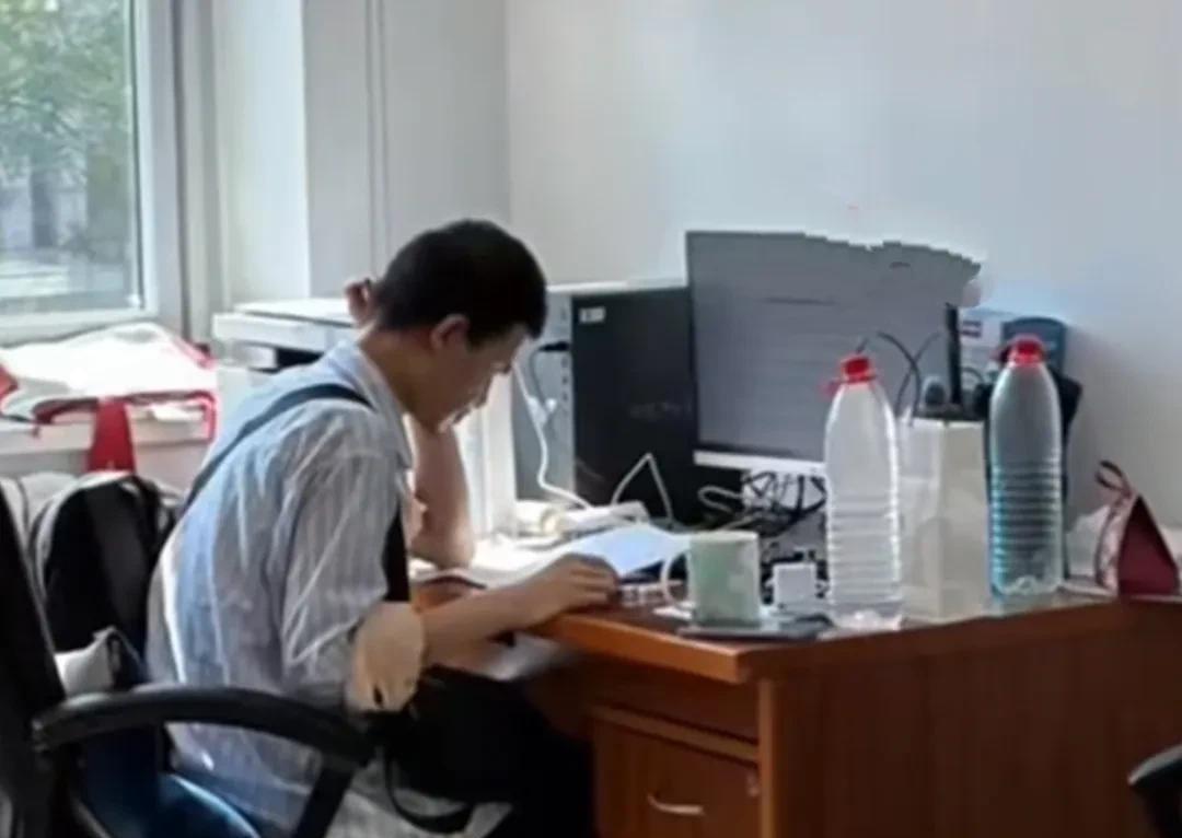 韦神在北大办公室工作的照片曝光，韦神坐在办公室一隅里，办公桌上放着电脑和打印机，