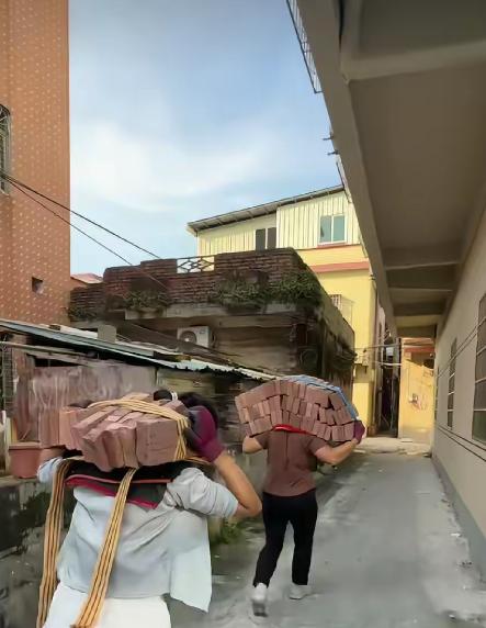 广东某居民楼下，搬运工大姐站在一堆红砖旁，像在等开场的“砖块巨兽”，准备开扛。她