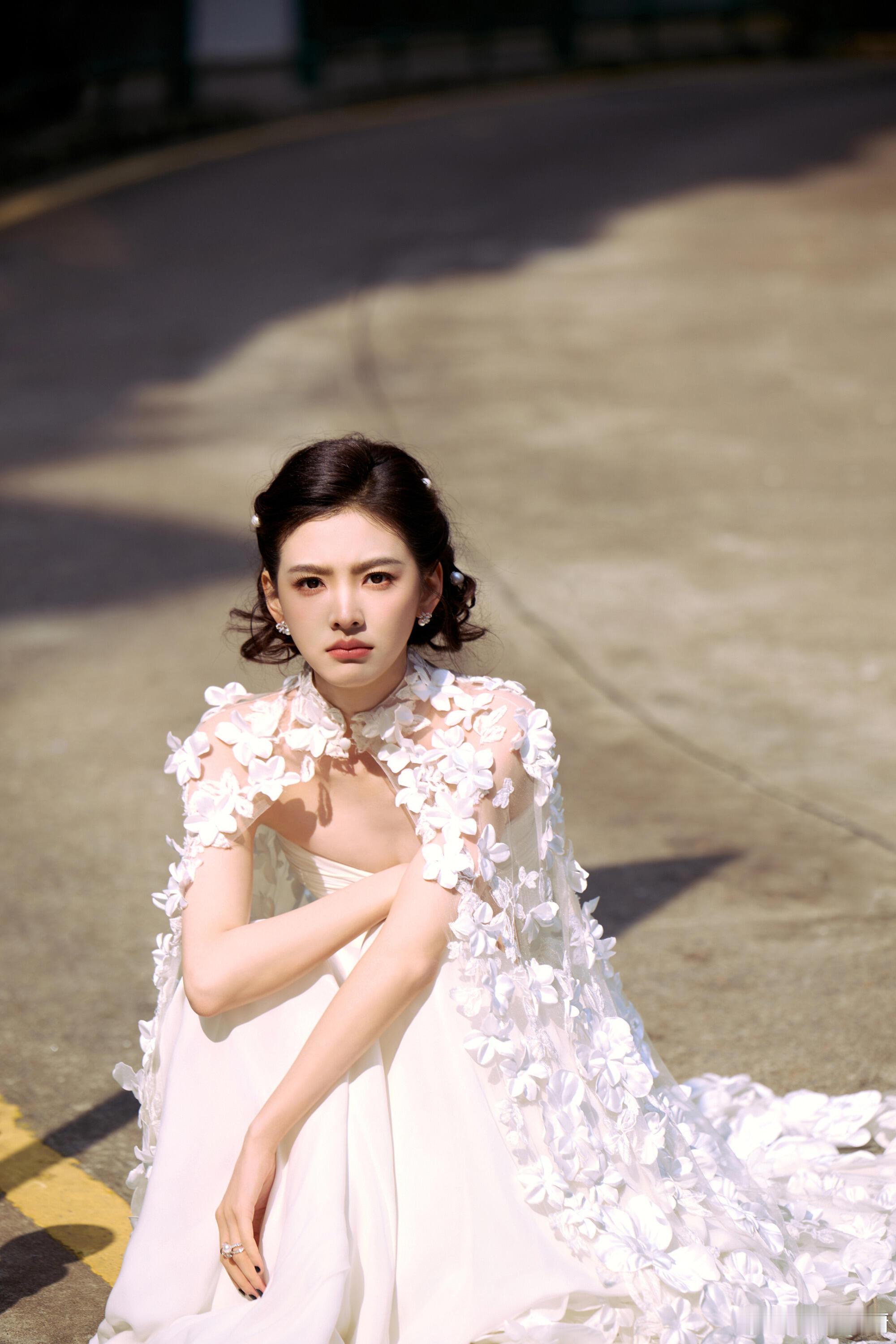 章若楠一袭纯白抹胸长裙裹着明媚气质，珍珠配饰衬出精致甜柔，街巷布景里的微风氛围感