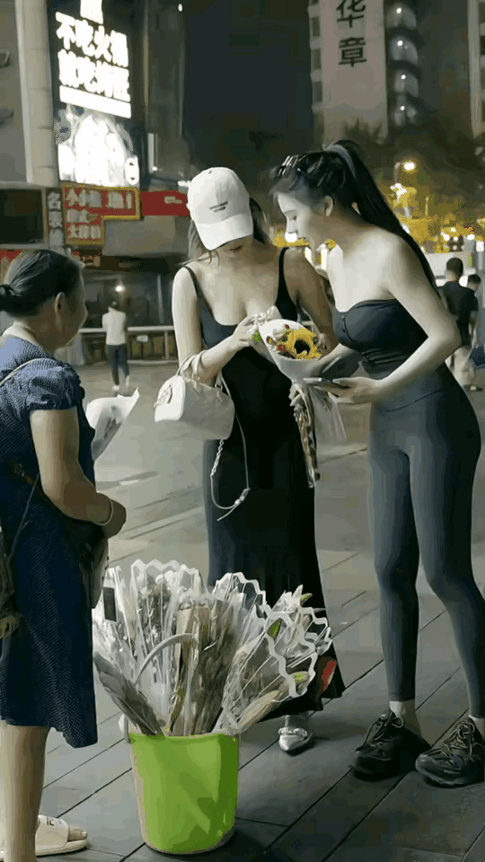 两个美女在街头买花，也算是成全了这个卖花的老大姐，细端详这两个美女，一个比一个漂