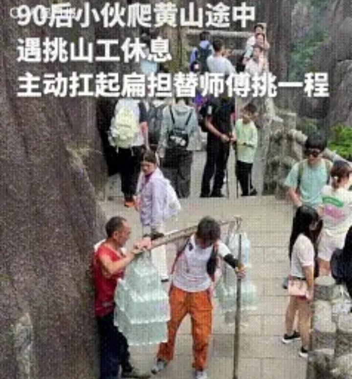 安徽黄山一名挑山工扛着两大捆矿泉水，累得倚靠山崖喘息。一名90后小伙途经见状主动