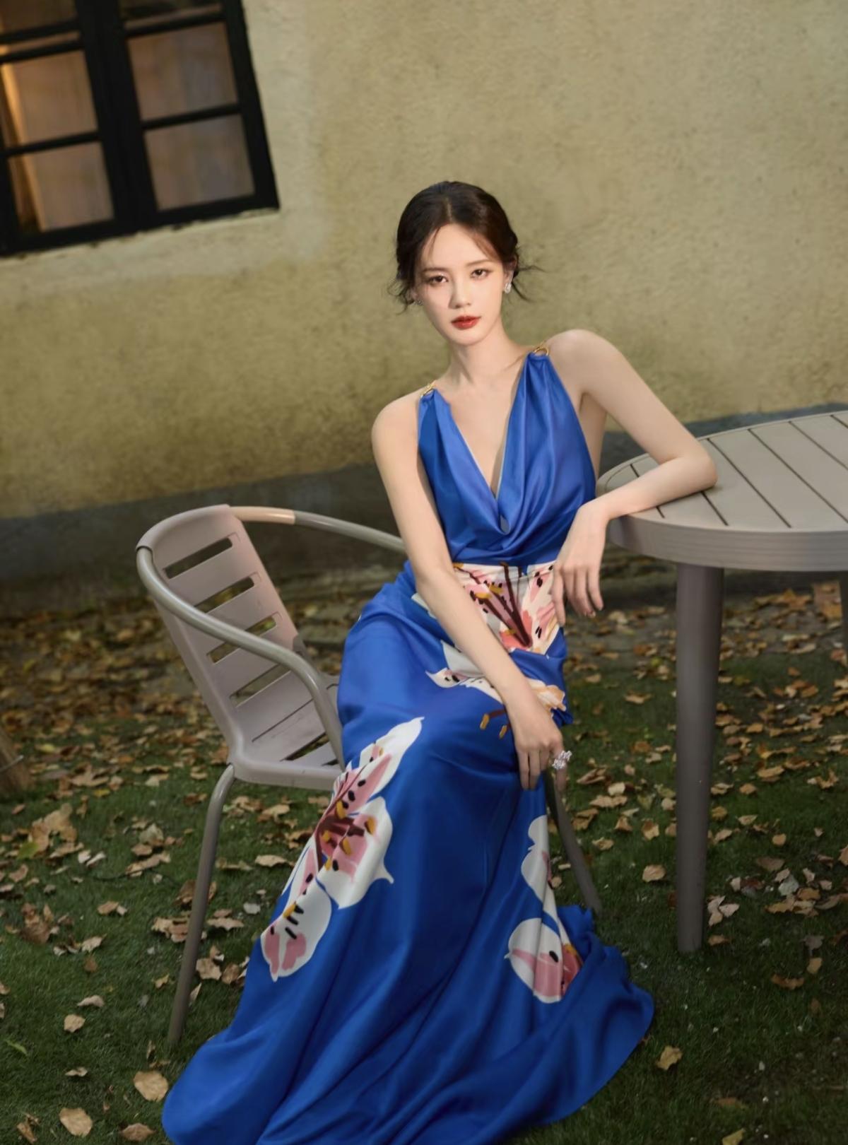 李一桐一袭宝蓝色挂脖长裙静立秋日庭院，缎面材质自带冷调光泽，腰间与裙摆的手绘花朵