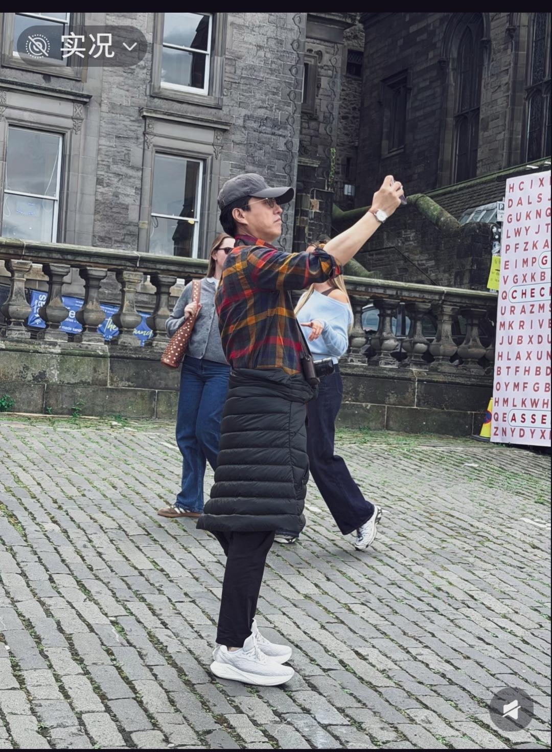 国外街头路人拍到靳东出来旅游。格纹衬衫，羽绒服直接系在腰上，戴着帽子墨镜，特有