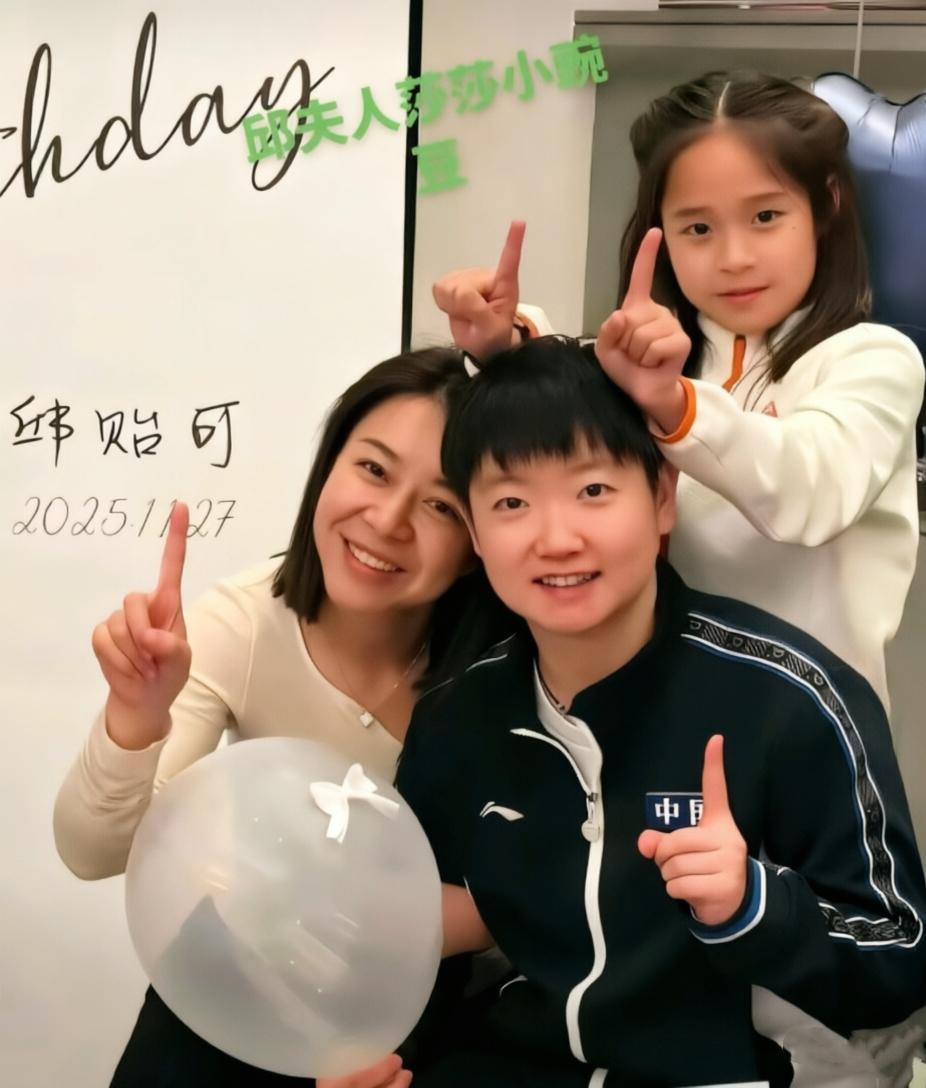 镜头中手持白色气球的孙颖莎短发利落，凤眼如虹，笑容甜美；一旁邱贻可的妻子文伟秀发