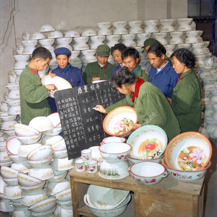 这是上世纪八十年代初湖南某搪瓷厂的生产现场照片，照片里，工人们围聚在摆满搪瓷碗、