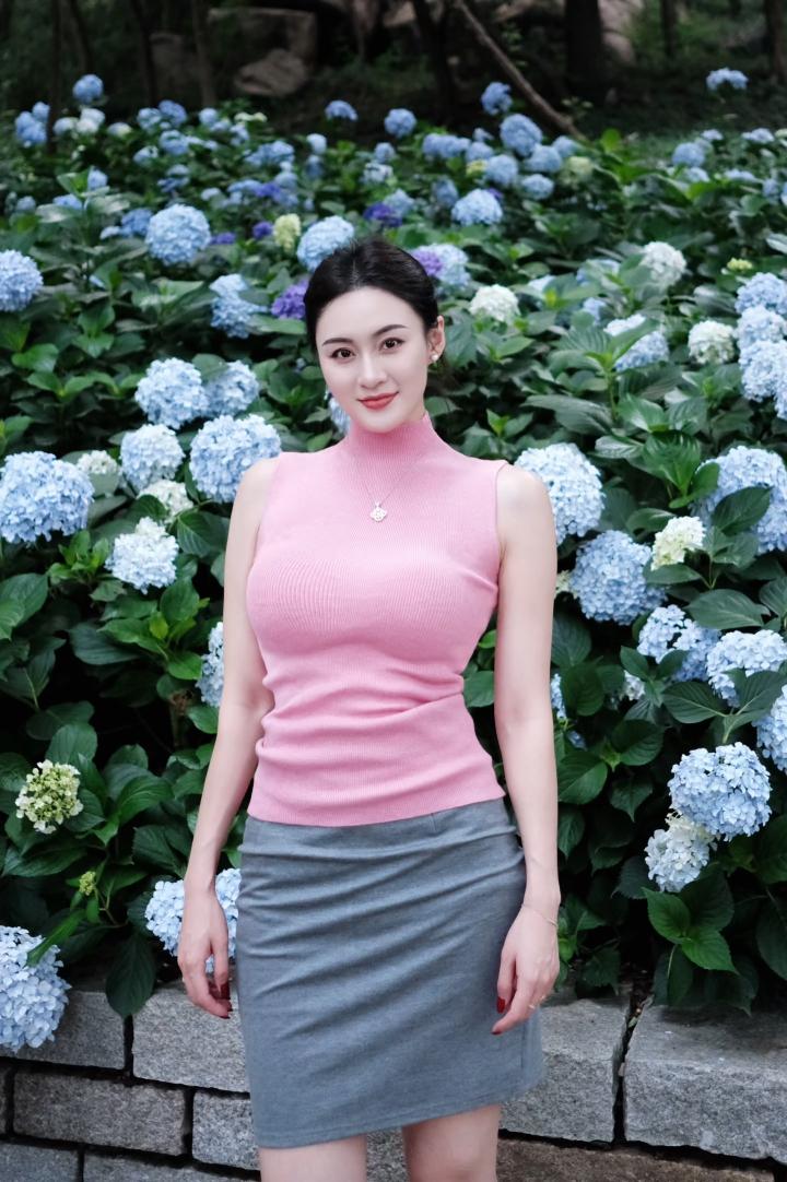 乌黑头发梳起，笑容明媚如春，颈间精致项链更添雅致。立于蓝白绣球花丛中，人花相映，