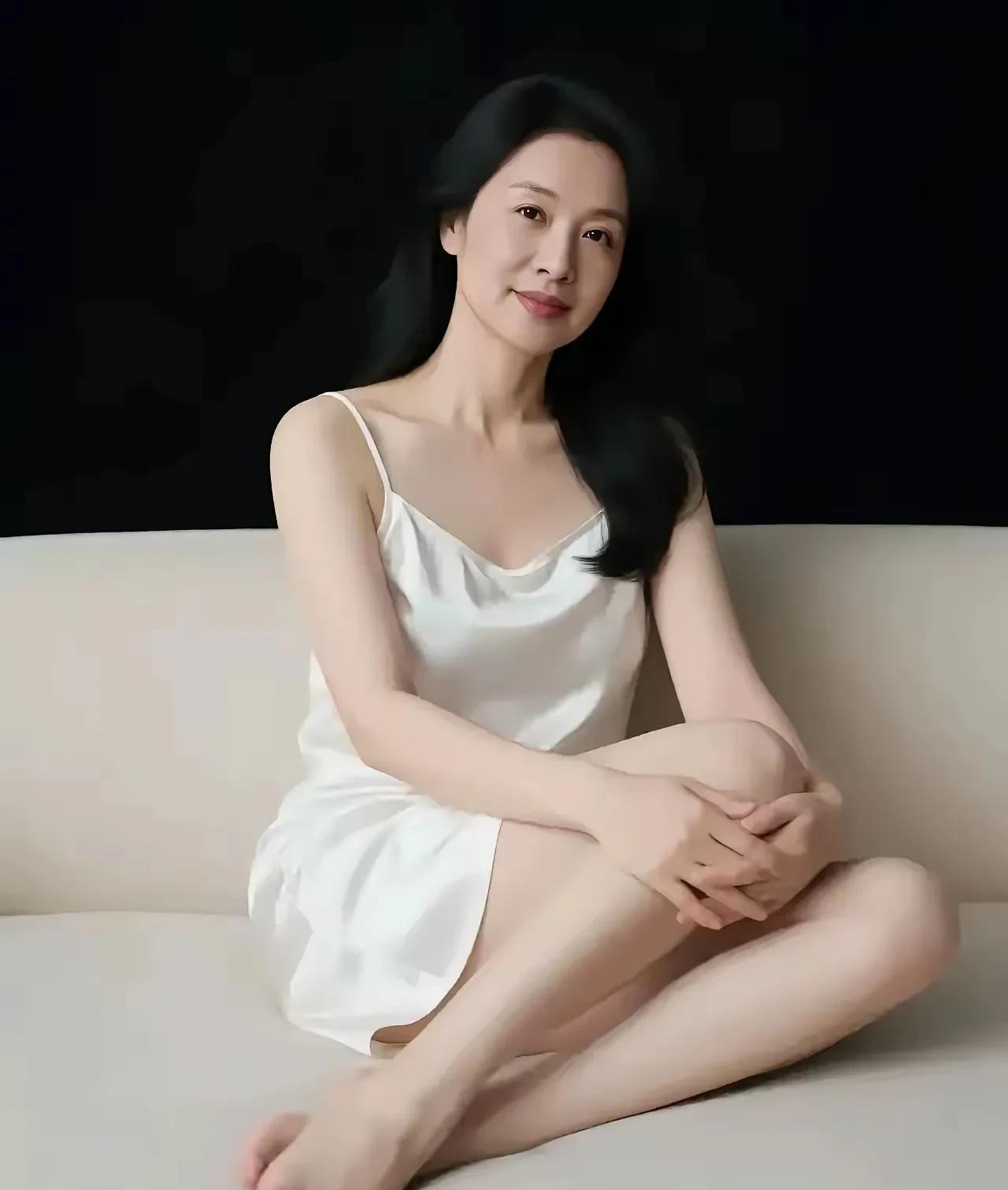 照片中的女性有一种温柔成熟之美，目测可能有五十岁，但保养的极好，一袭白色吊带，衬